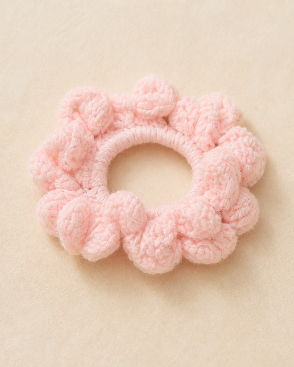 Blush-pink crochet scrunchie with a wrapped center ring and dense layered ruffled loops