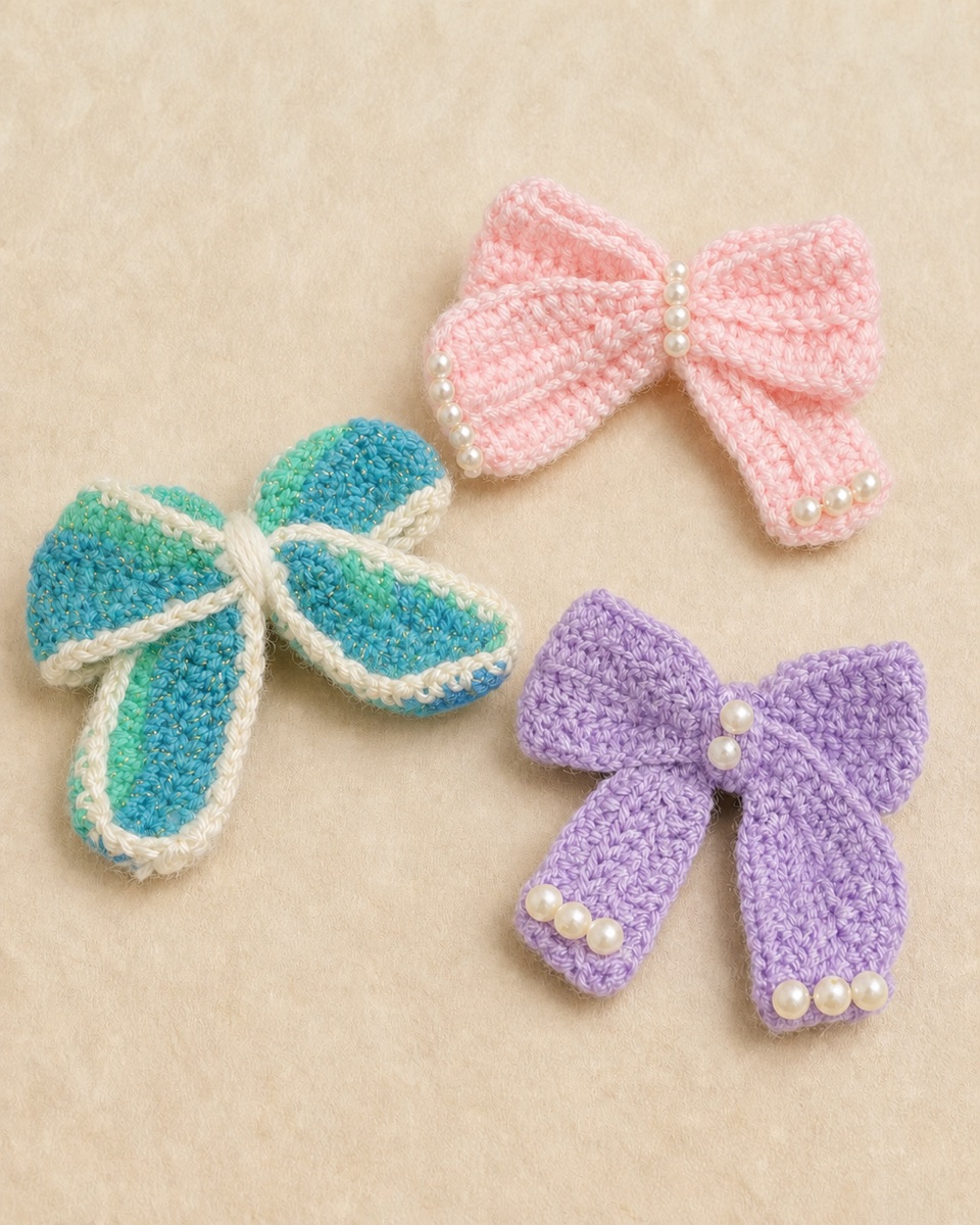Pink and lavender crocheted bows with round white bead accents beside an aqua bow with cream edging